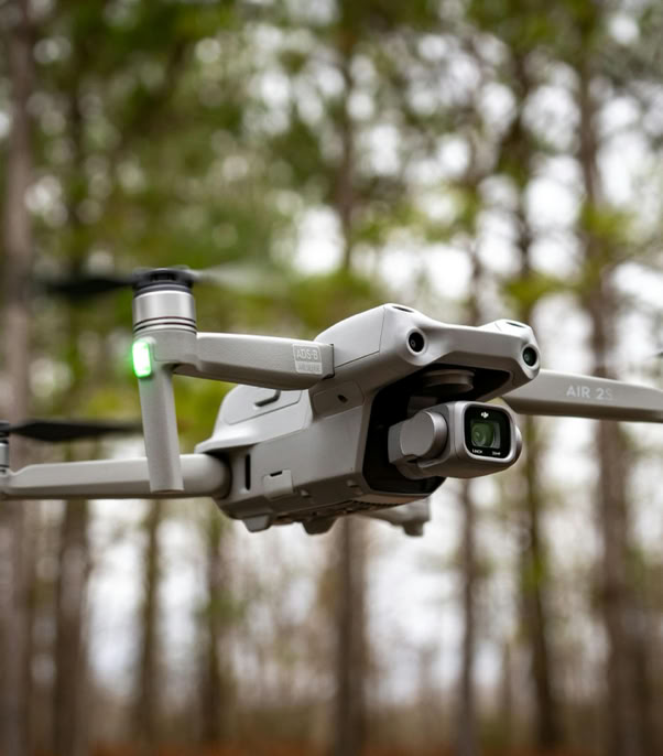 Close-up of a drone in midair with trees in the background, showcasing technology and nature.